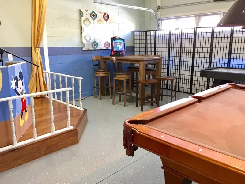 Game room – A pool table in a room with a staircase, a table with chairs, and a Mickey Mouse-themed decoration.