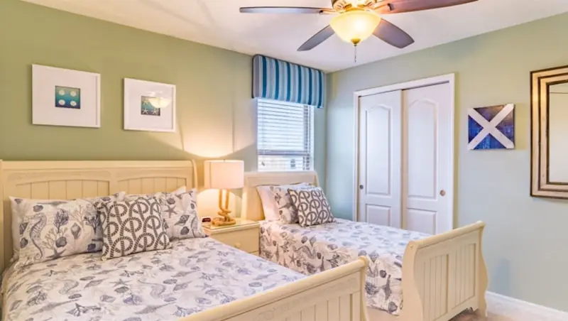 Room – A bedroom with two twin beds, a ceiling fan, a window with blinds, and a door.