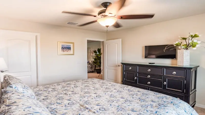 2nd floor king bedroom – A bedroom with a bed, a dresser, a ceiling fan, a television, and a door leading to another room.