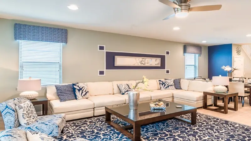 parlor – A living room with a beige sectional sofa, a glass coffee table, patterned rugs, and a ceiling fan.