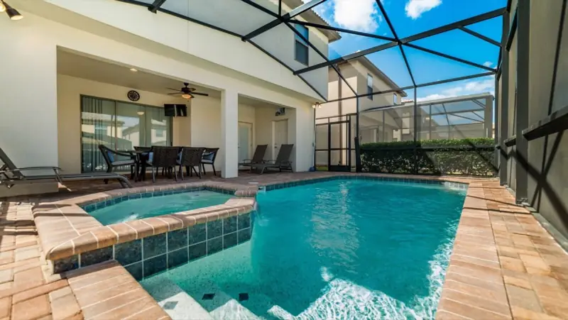 Hot Tub, Pool, Outside TV, and Seating (always there) – A swimming pool with two hot tubs, surrounded by a covered patio area with seating and a ceiling fan.